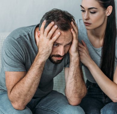 young woman supporting depressed frustrated boyfriend sitting on couch